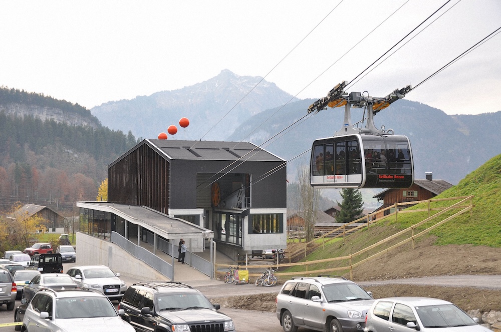 Talstation der Seilbahn Bezau mit ausfahrender Gondel und parkenden Autos im Vordergrund