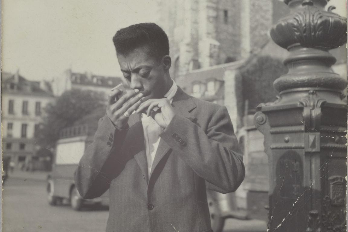Black and white photo of James Baldwin lighting a cigarette.