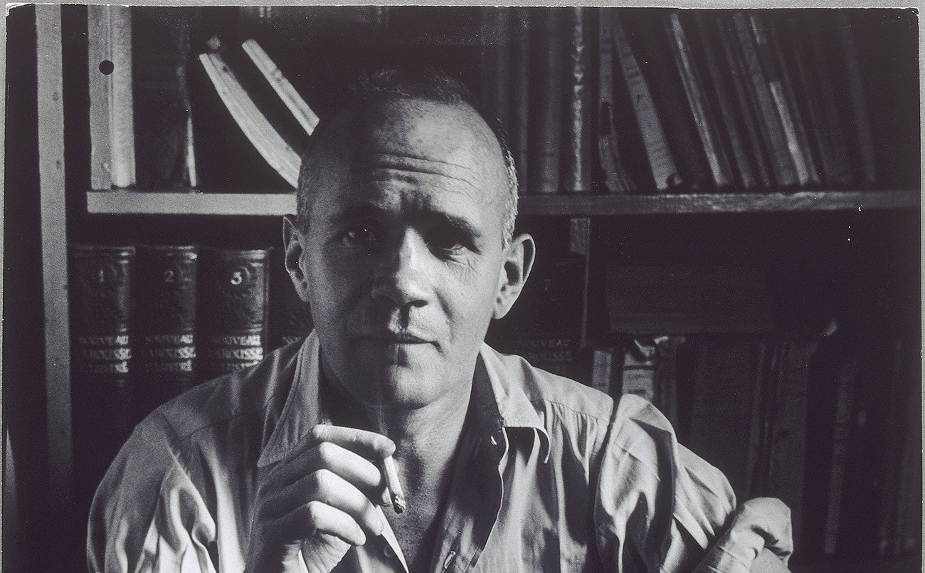 Black and white photo of Jean Genet facing camera and smoking a cigarette.