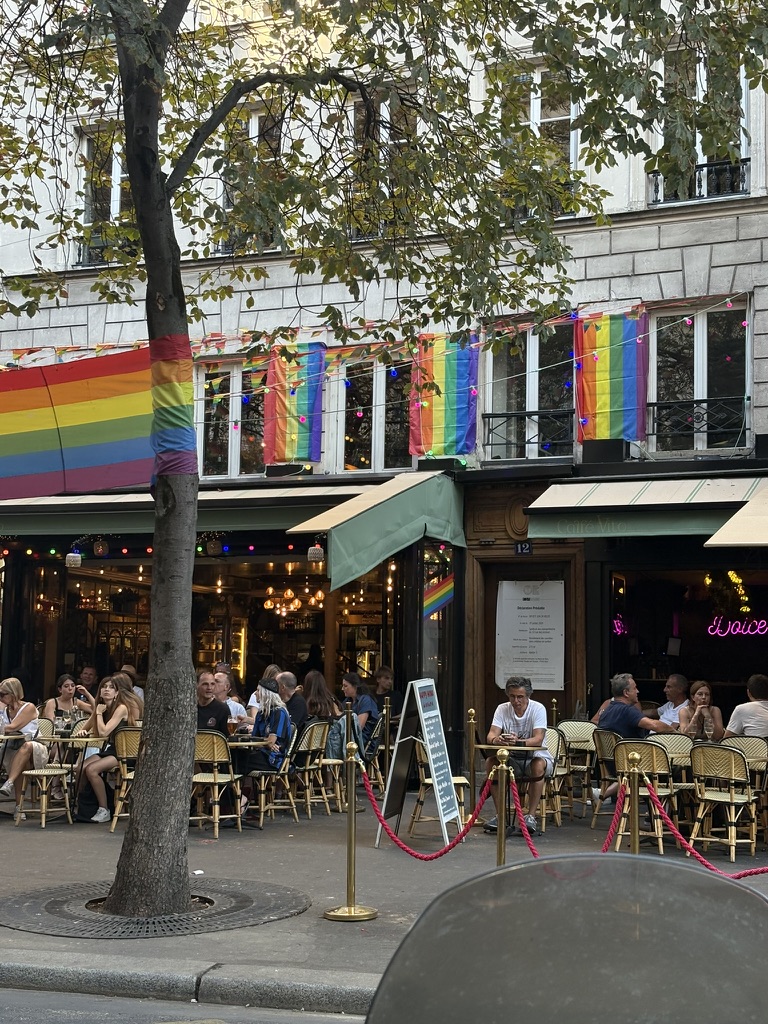Front facade of the Café Vito bar in Paris, with patio and rainbow flags hanging above the entrance.