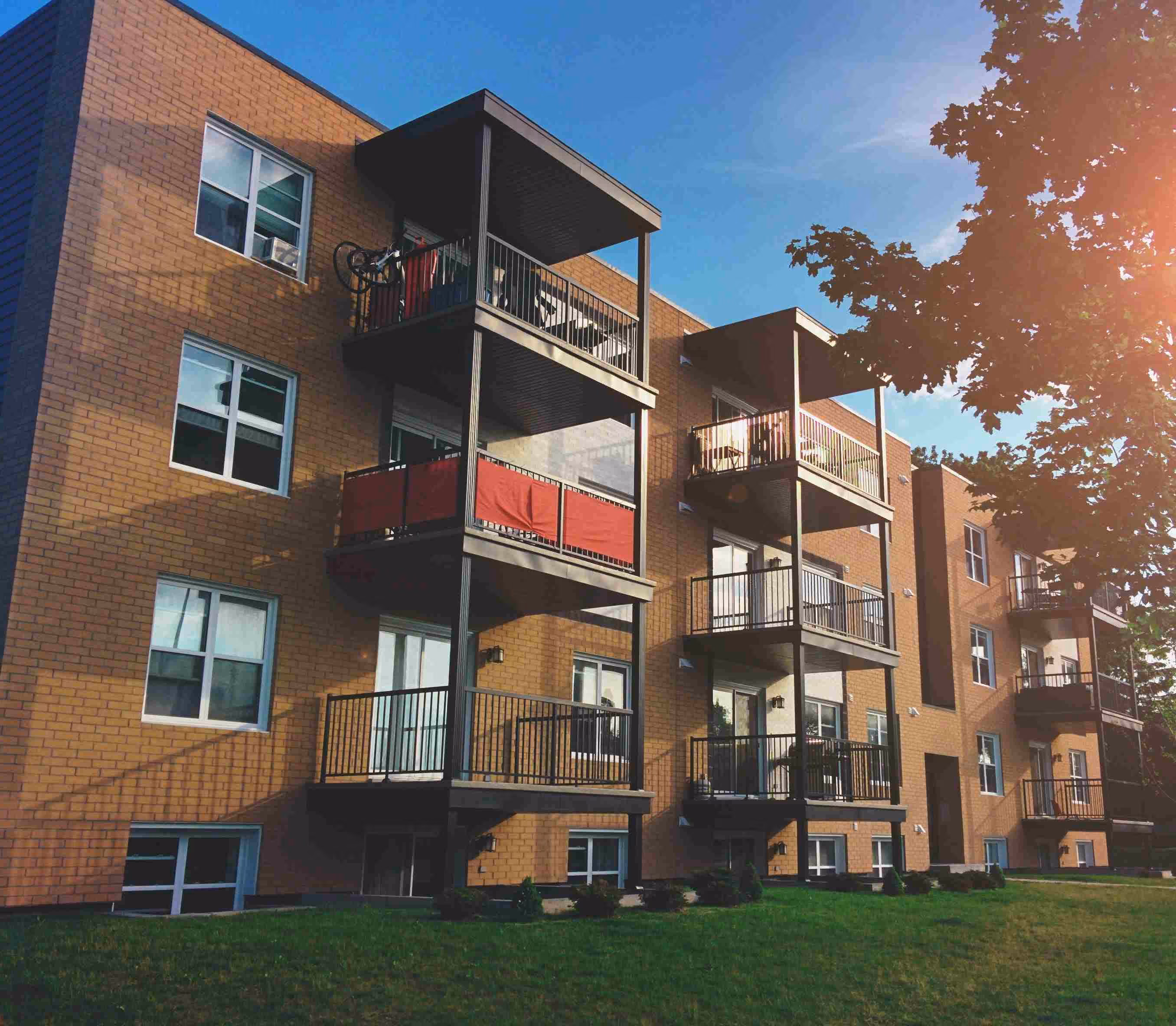 Modernes Mehrfamilienhaus in Mainburg mit energieeffizienter Klinkerfassade, schwarzen Balkonen und gepflegter Grünfläche bei strahlendem Sonnenschein.