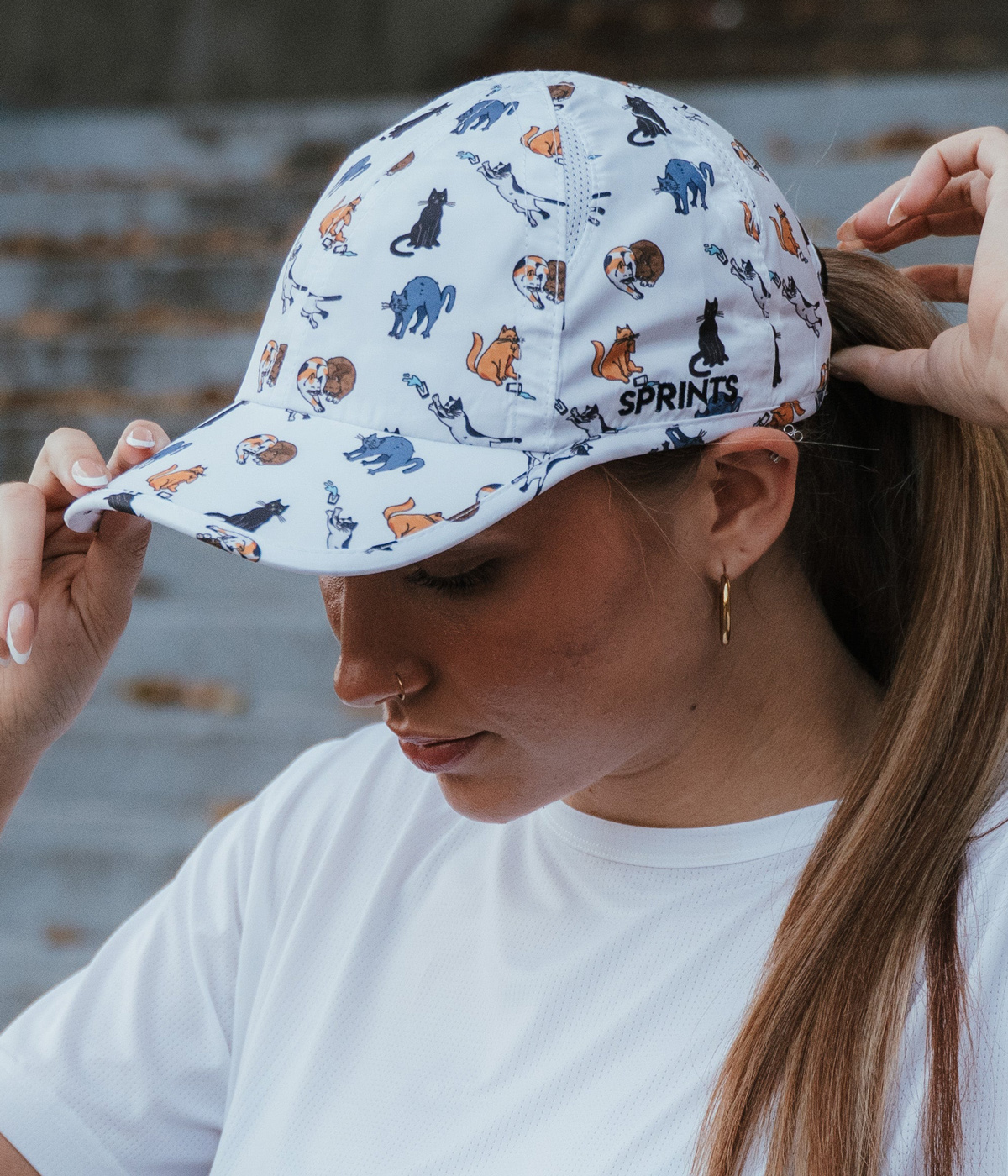 Person wearing a white cap with small colorful cat illustrations and the word 'SPRINTS' on the side.