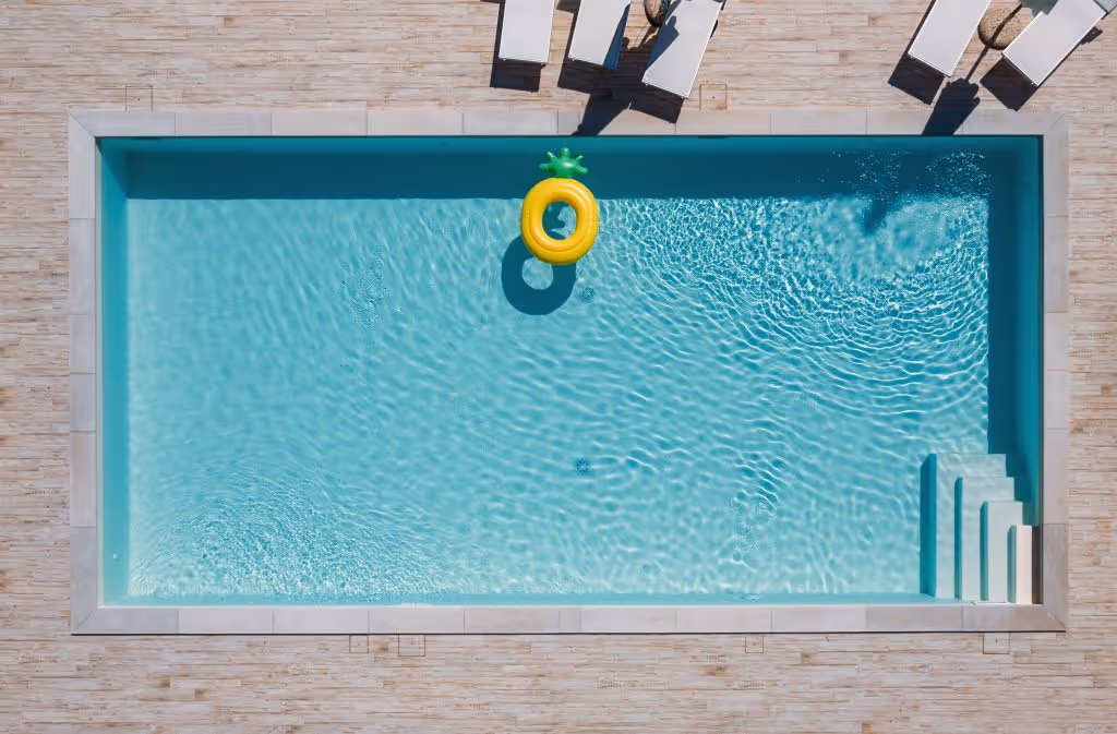 Large rectangular swimming pool with a pineapple floatie near the side. Five sunbeds are near the pool, too.