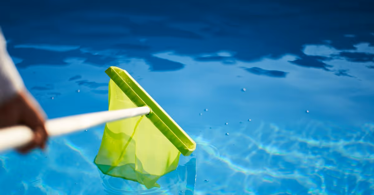 Close-up of someone using a green skimmer net with a white pole in a swimming pool. However, the water is clear.