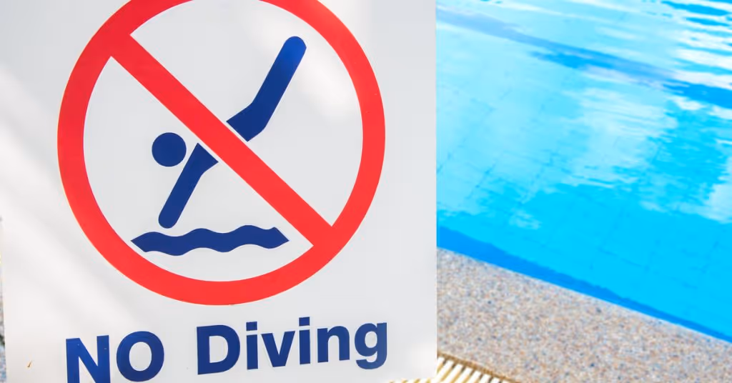 A “no diving” sign is near a swimming pool. The sign has a red circle with a diagonal line crossing out a diving figure.