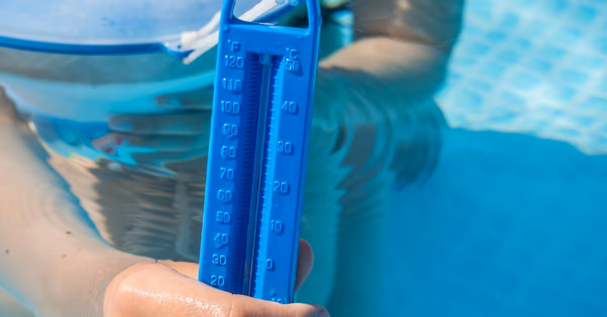 A close-up of someone holding a blue thermometer in a swimming pool. The thermometer is attached to a blue floating disc.