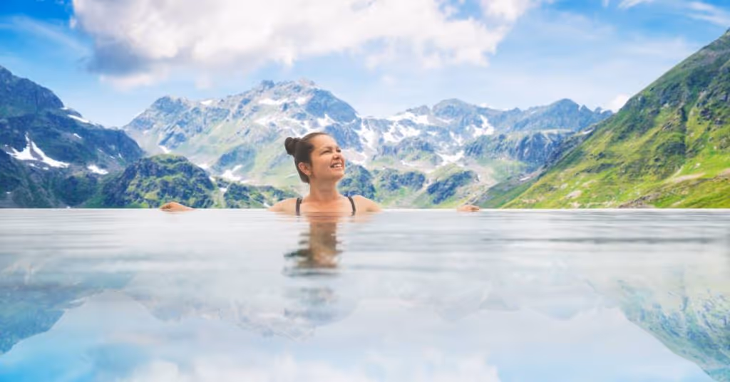 A woman near the edge of an infinity pool. She's smiling and looking toward the right. Mountains are in the background.