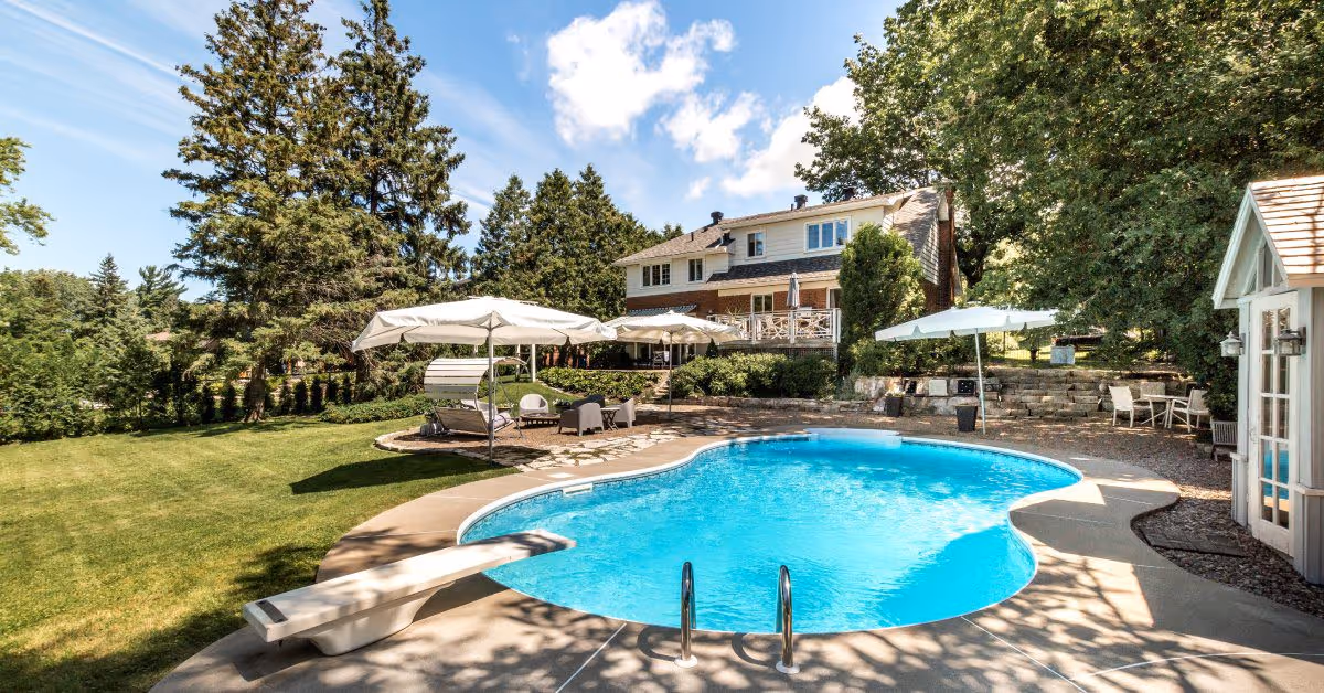 A close-up of a home's backyard with a large inground custom swimming pool. There are two sitting areas with an umbrella.