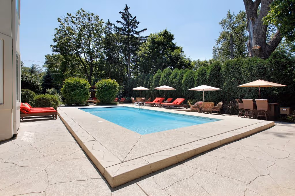A luxurious residential pool. There are red lounge chairs, cream umbrellas, and additional table seating.