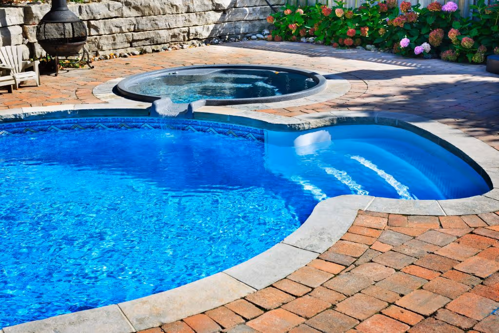 A close-up of a residential pool and hot tub. The pool is irregular in shape, and the hot tub is circular.