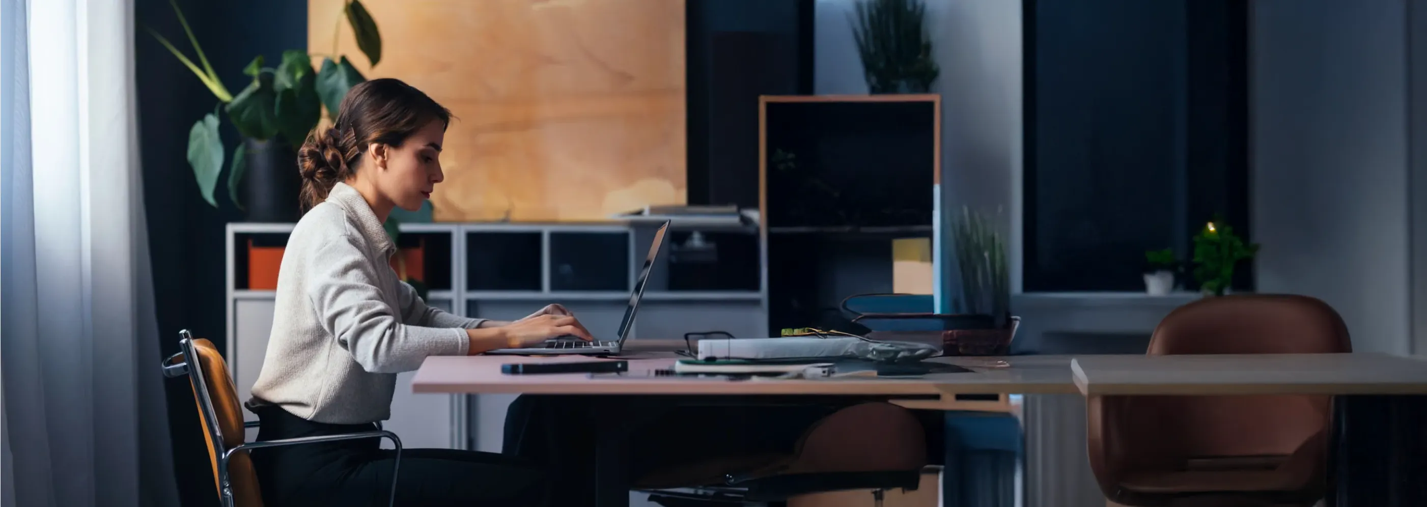 Une femme travaille seule sur son ordinateur dans un bureau en soirée, illustrant l’usage d’une solution métier dédiée à la gestion des paiements.