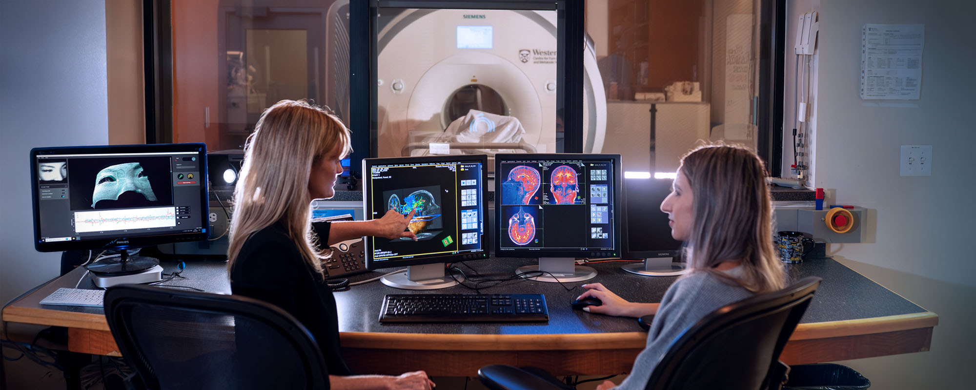 Two people looking a the brain though a computer with CT machine in the background.