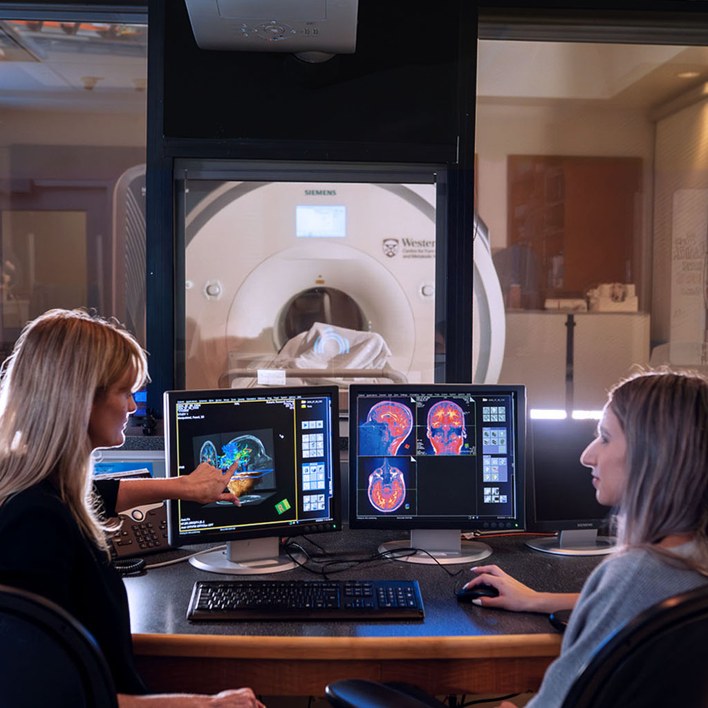 Two people looking a the brain though a computer with CT machine in the background.
