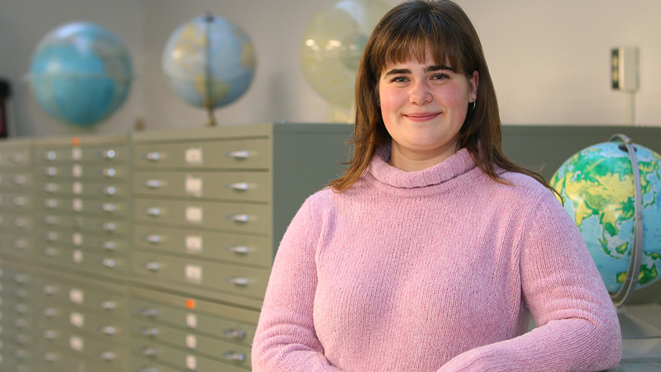 Sophia Slabon sourrounded by globes in the Map and Data Centre at Western, where she works part-time while pursuing her geography degree