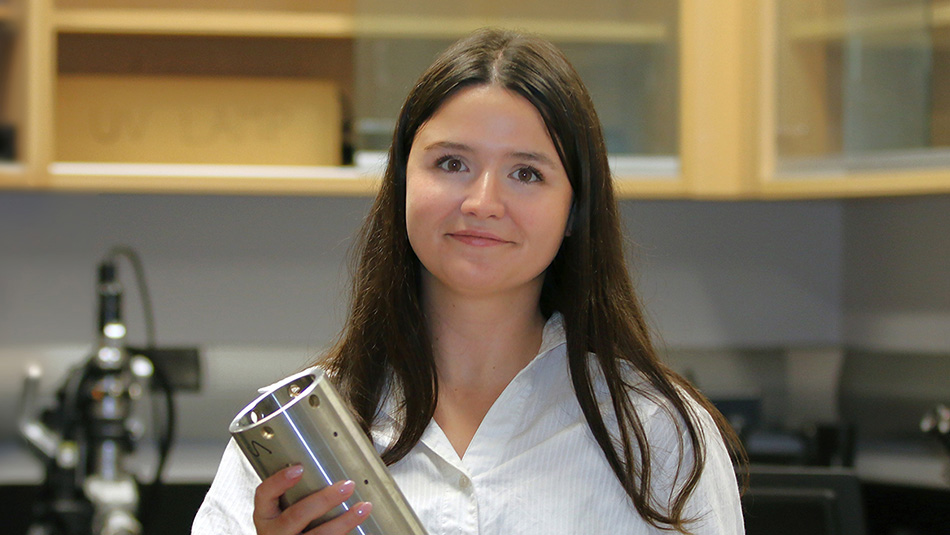 Jessie McDonald in front of a microcope, holding a steel module that researchers pulled from the proposed deep geological repository site