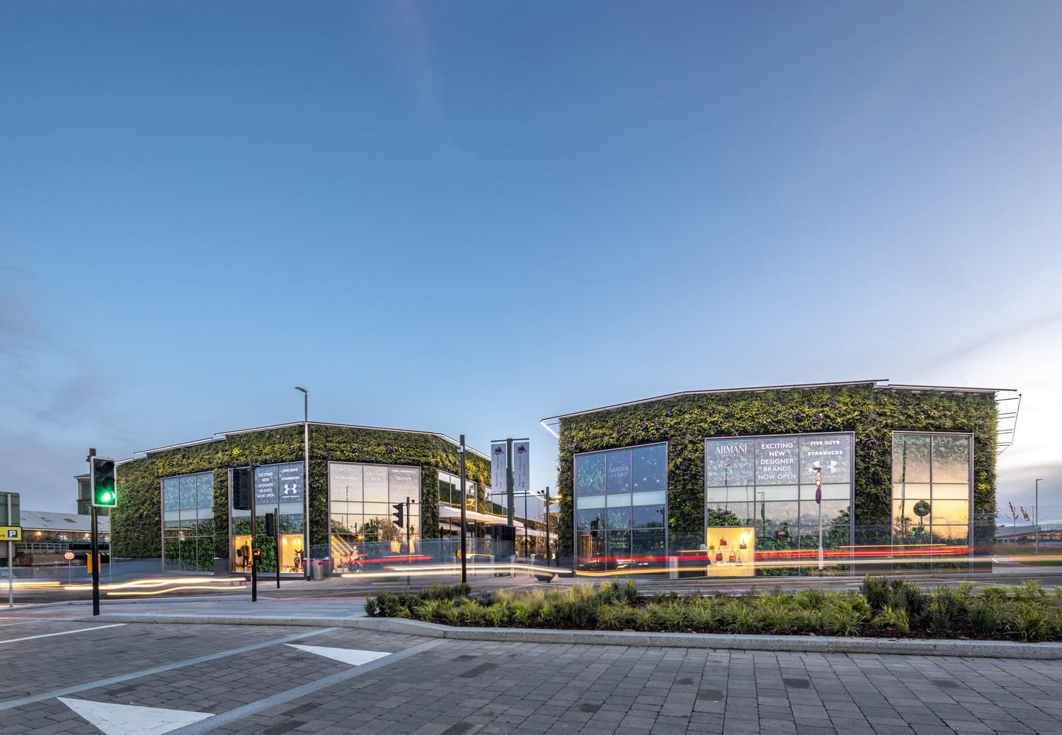McArthurGlen Designer Outlet at dusk, with green living walls on the shop fronts