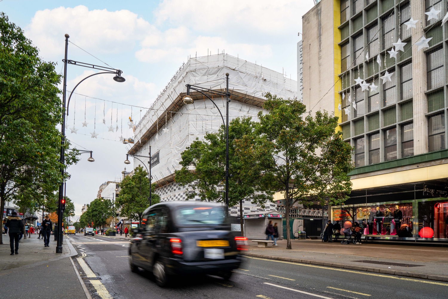 318 Oxford Street under refurbishment, wrapped in scaffolding, with a black cab passing
