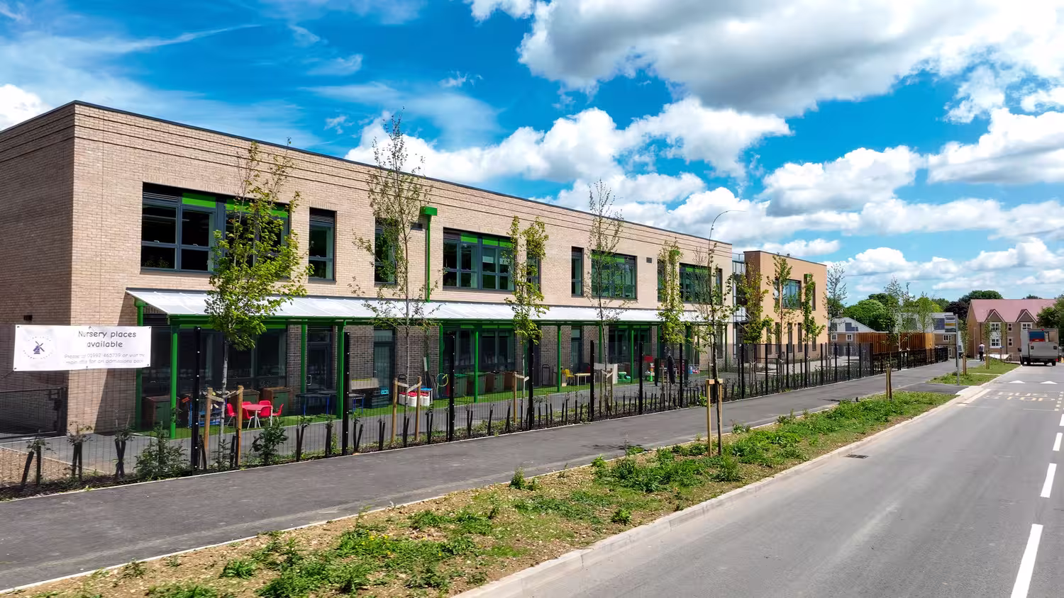 An image of the outside of High Leigh Primary School, with blue sky and clouds. The school has sandstone brick work and bright green detailing around the windows. There are no people or children in the photo.