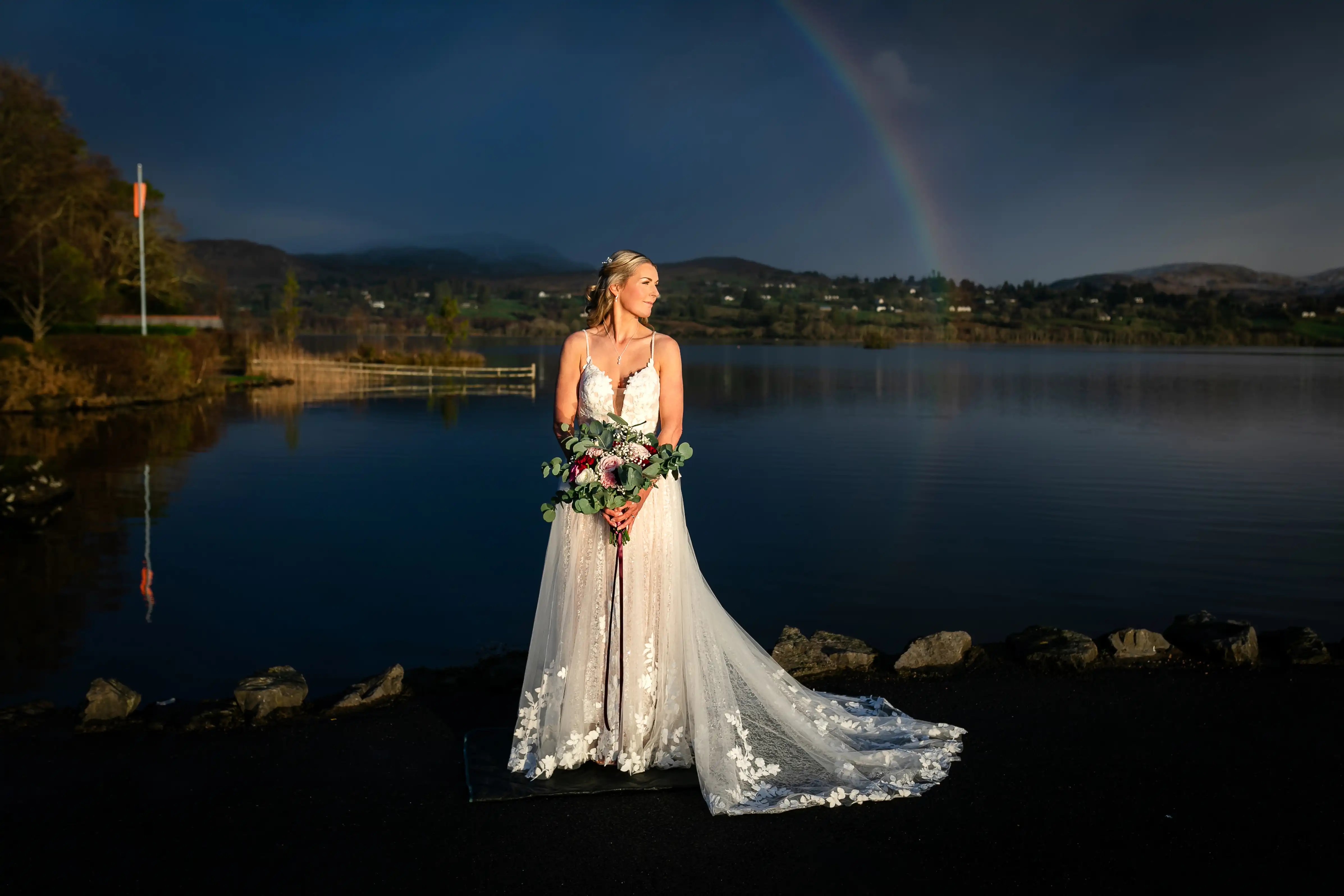 Bride in dress holding flowers in front of a lake