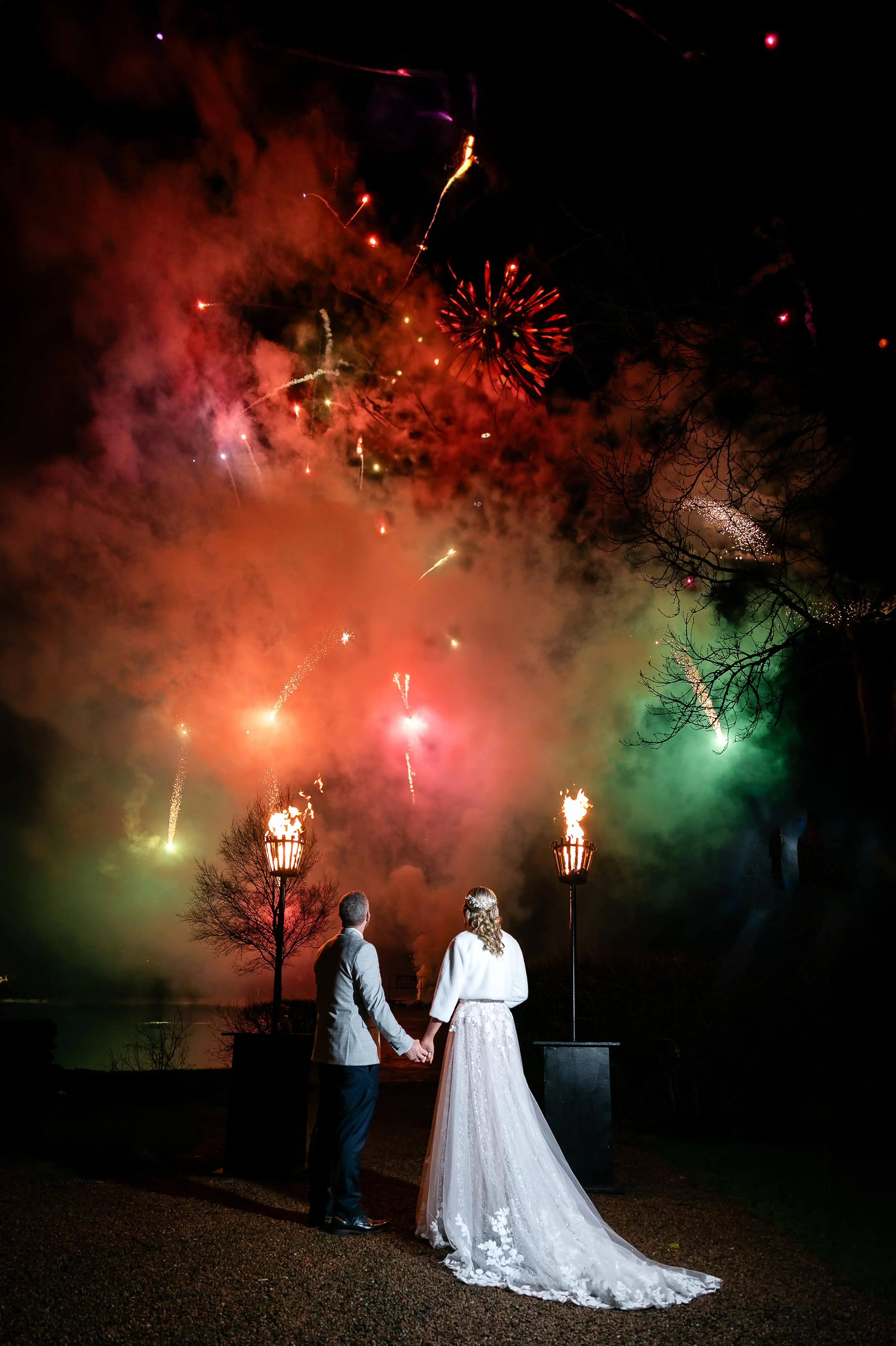 Bride and groom holding hands in front of fireworks
