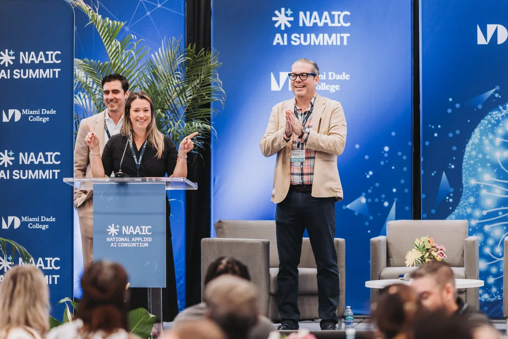 Speakers at a podium and on stage during the NAAIC AI Summit at Miami Dade College.