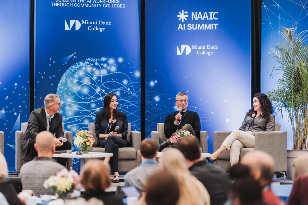 Four panelists seated on stage during the NAAIC AI Summit at Miami Dade College, with an audience in the foreground.