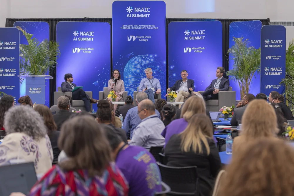 Panel discussion at NAAIC AI Summit hosted by Miami Dade College, with five speakers seated on stage facing an audience.