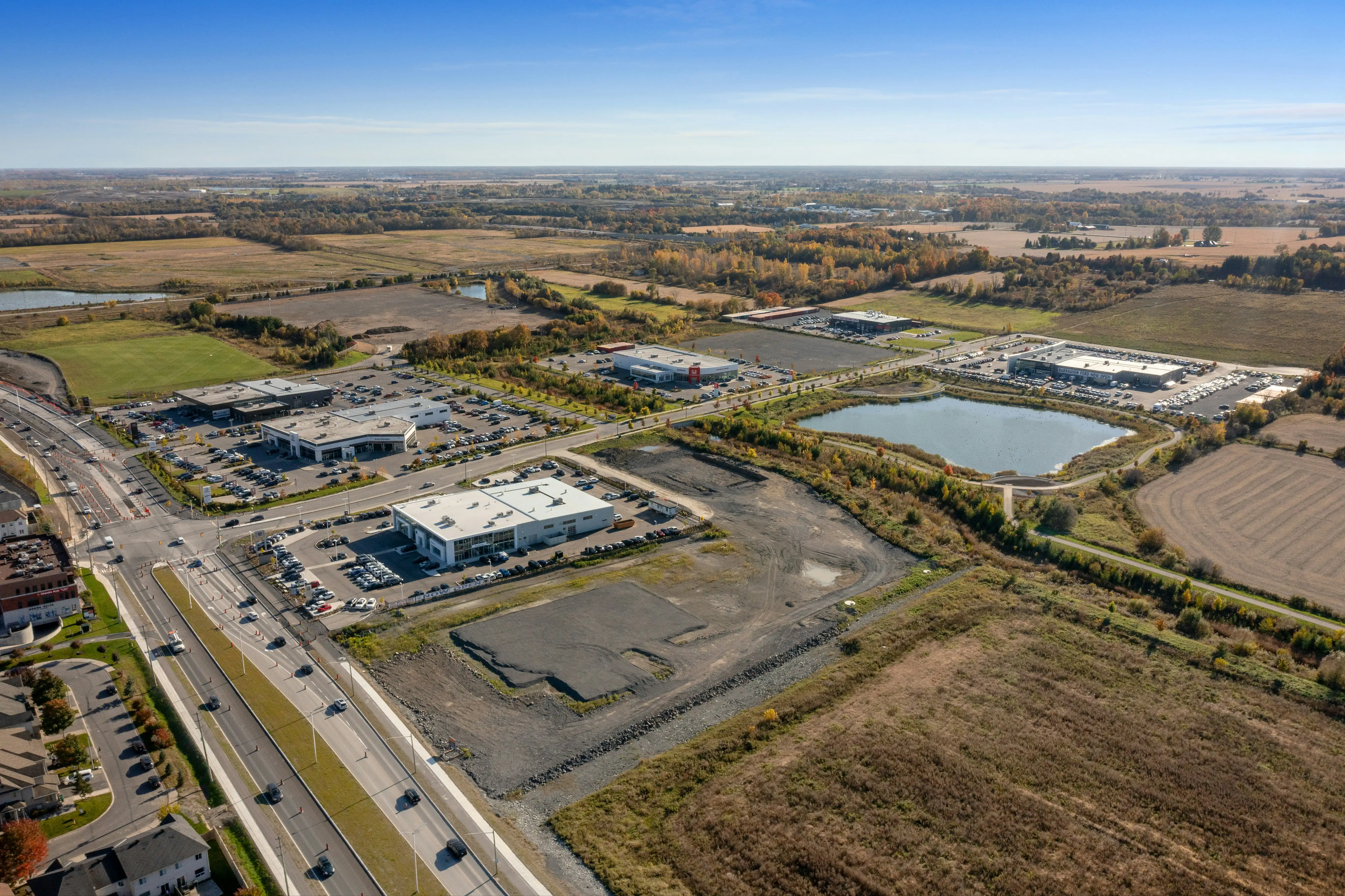Vue aérienne d'une zone industrielle avec plusieurs bâtiments, parkings, routes et un étang.
