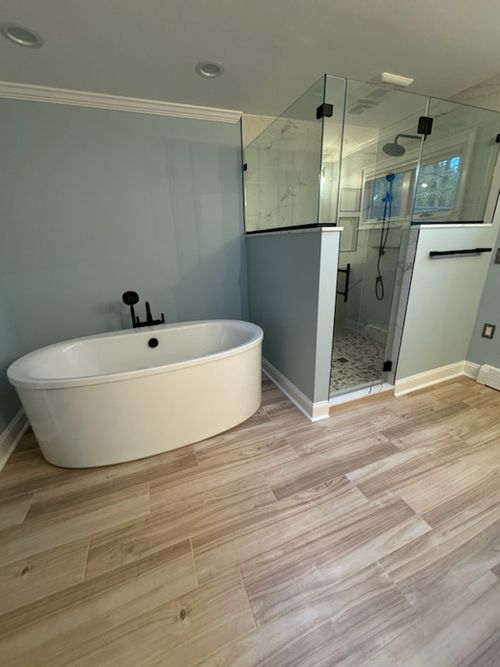 Bathroom remodel with freestanding soaking tub, glass shower, and wood-look porcelain tile flooring.