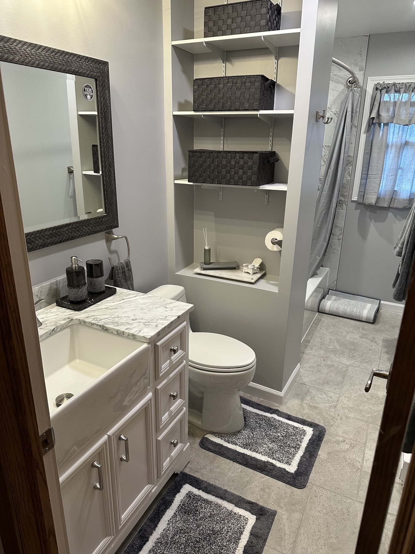 Finished Hampton, NJ bathroom with a white farmhouse-front vanity, marble-look countertop, framed mirror and built-in shelving above the toilet