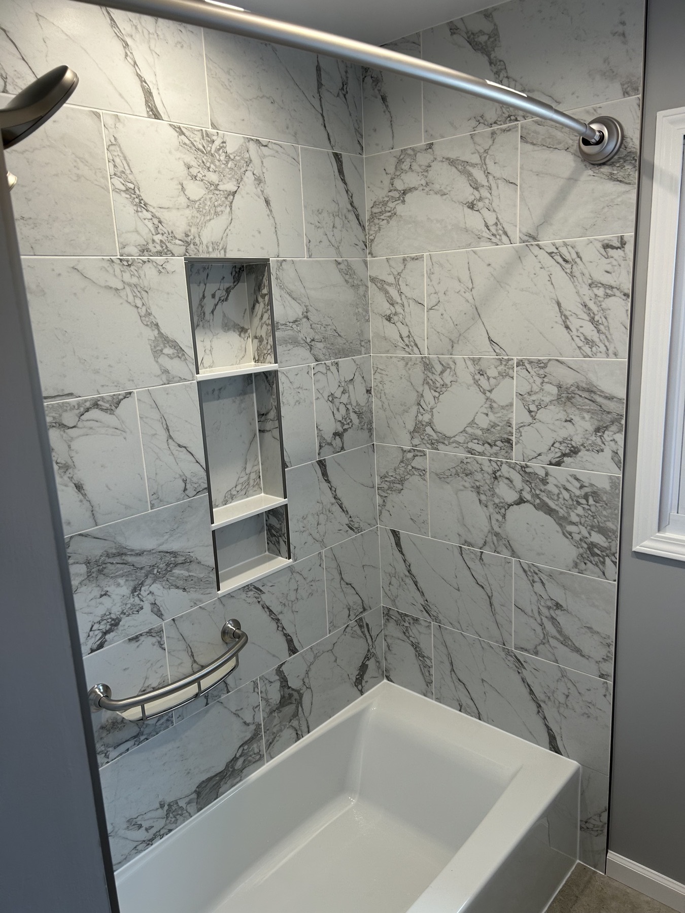 Carrara-look 12 by 24 porcelain tub surround in a Hampton, NJ bathroom with a recessed two-compartment niche and a brushed nickel grab bar