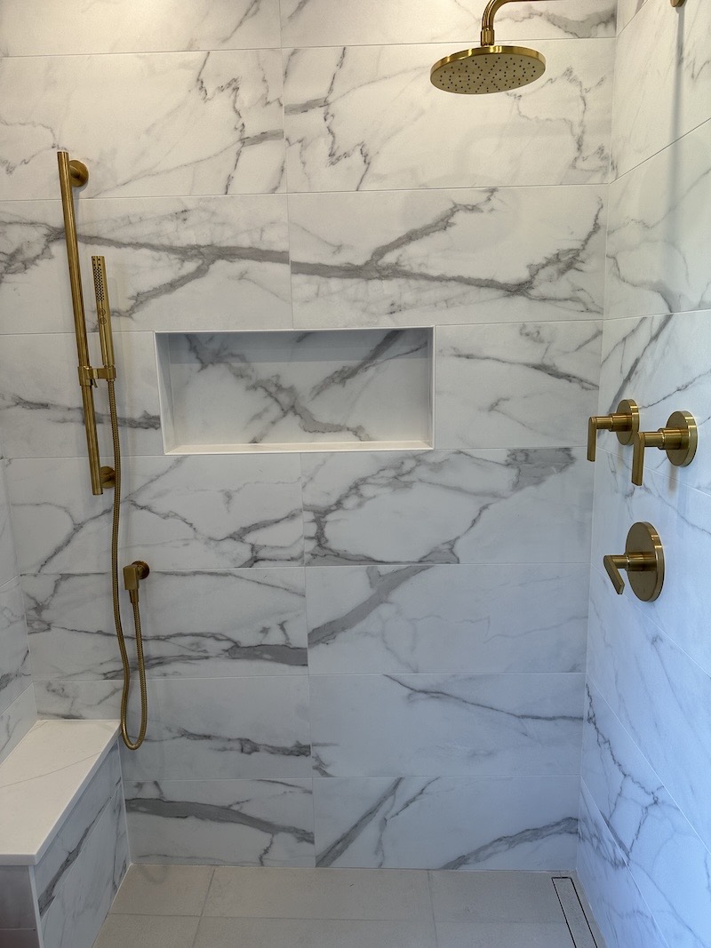 Marble-look porcelain shower in a Pittstown, NJ bathroom with brushed brass fixtures, a recessed niche and a built-in bench