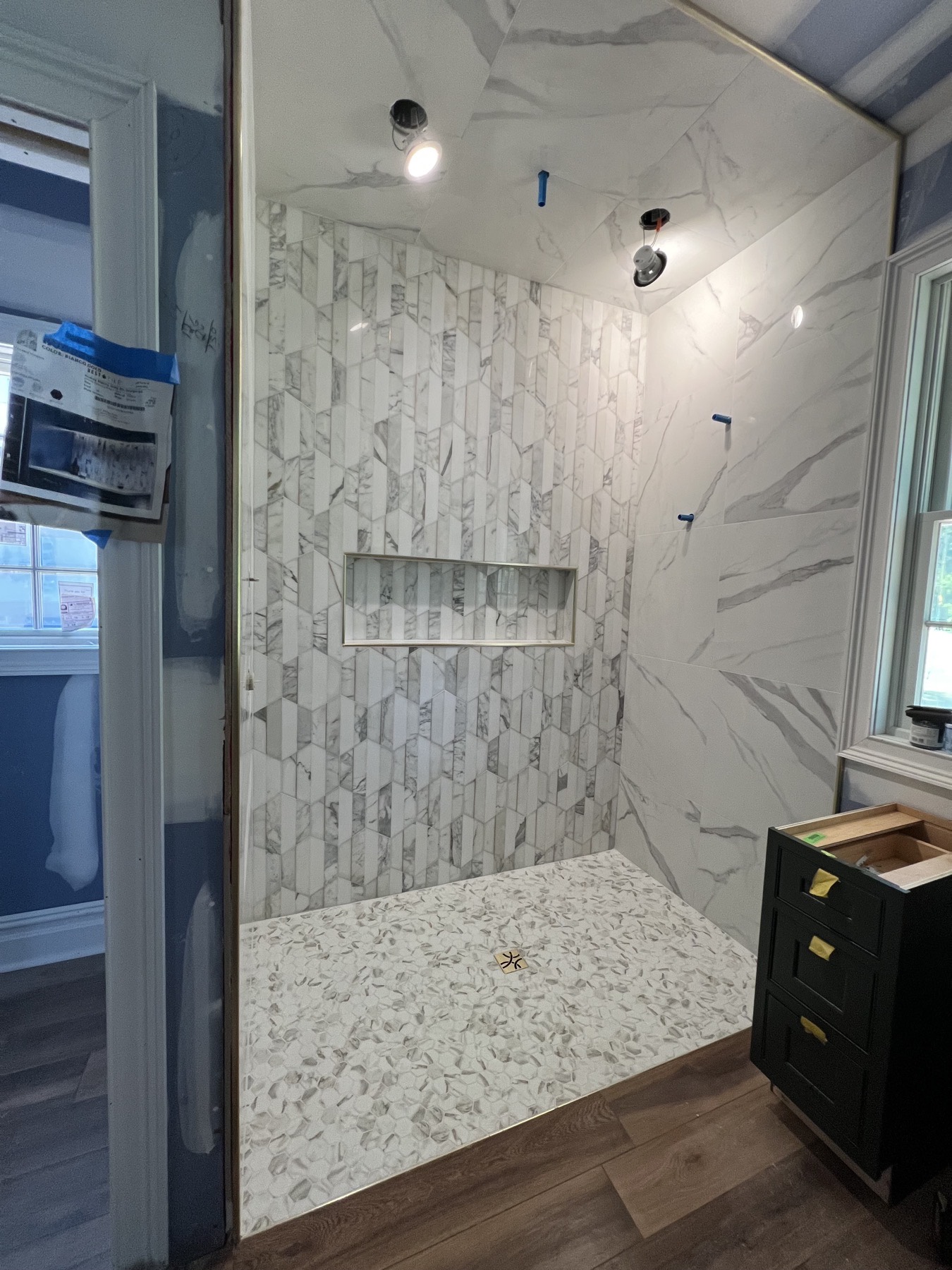 Curbless shower under construction in Whitehouse Station, NJ with an elongated picket marble-look accent wall, hexagon mosaic pan and brass trim