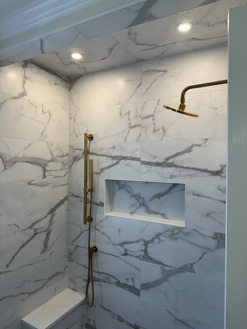 Brushed brass rain shower head and hand shower on a slide bar mounted on large-format marble-look porcelain tile in Pittstown, NJ