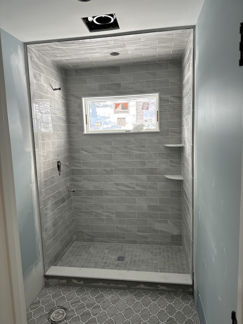 Walk-in shower in Somerville, NJ tiled in grey marble-look plank with an inset window, corner shelves and a square mosaic shower pan