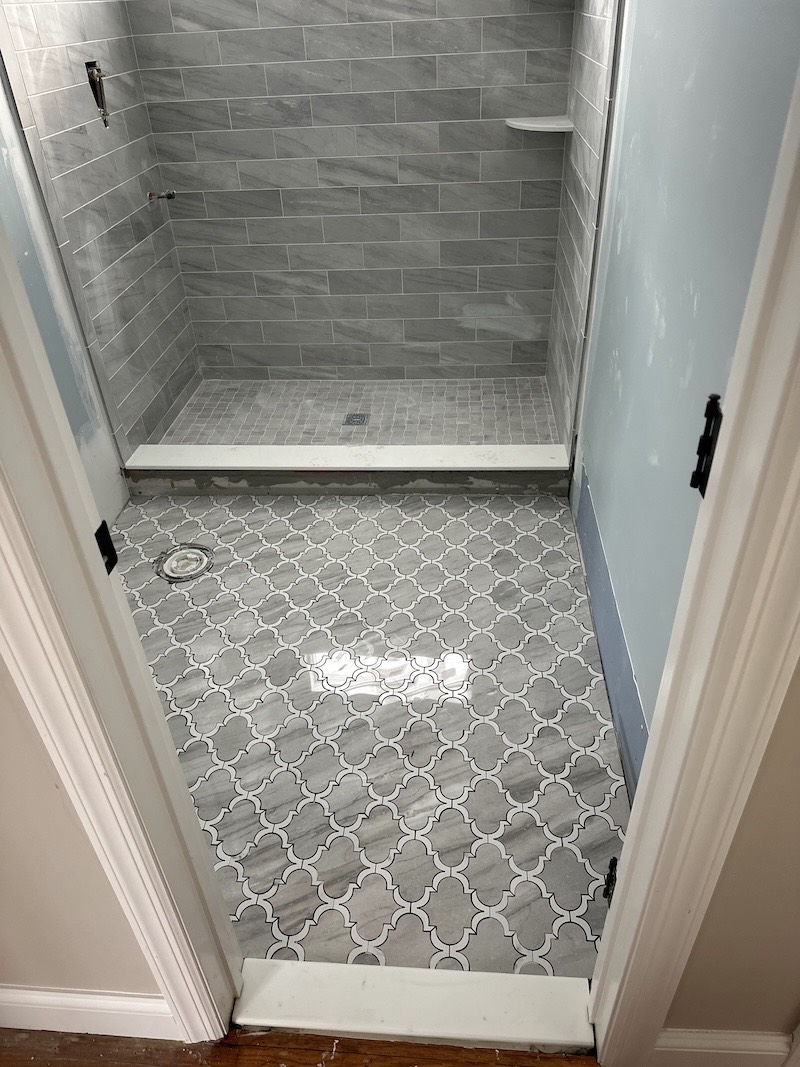 Grey arabesque lantern mosaic bathroom floor in Somerville, NJ, leading into a walk-in shower tiled in grey marble-look plank