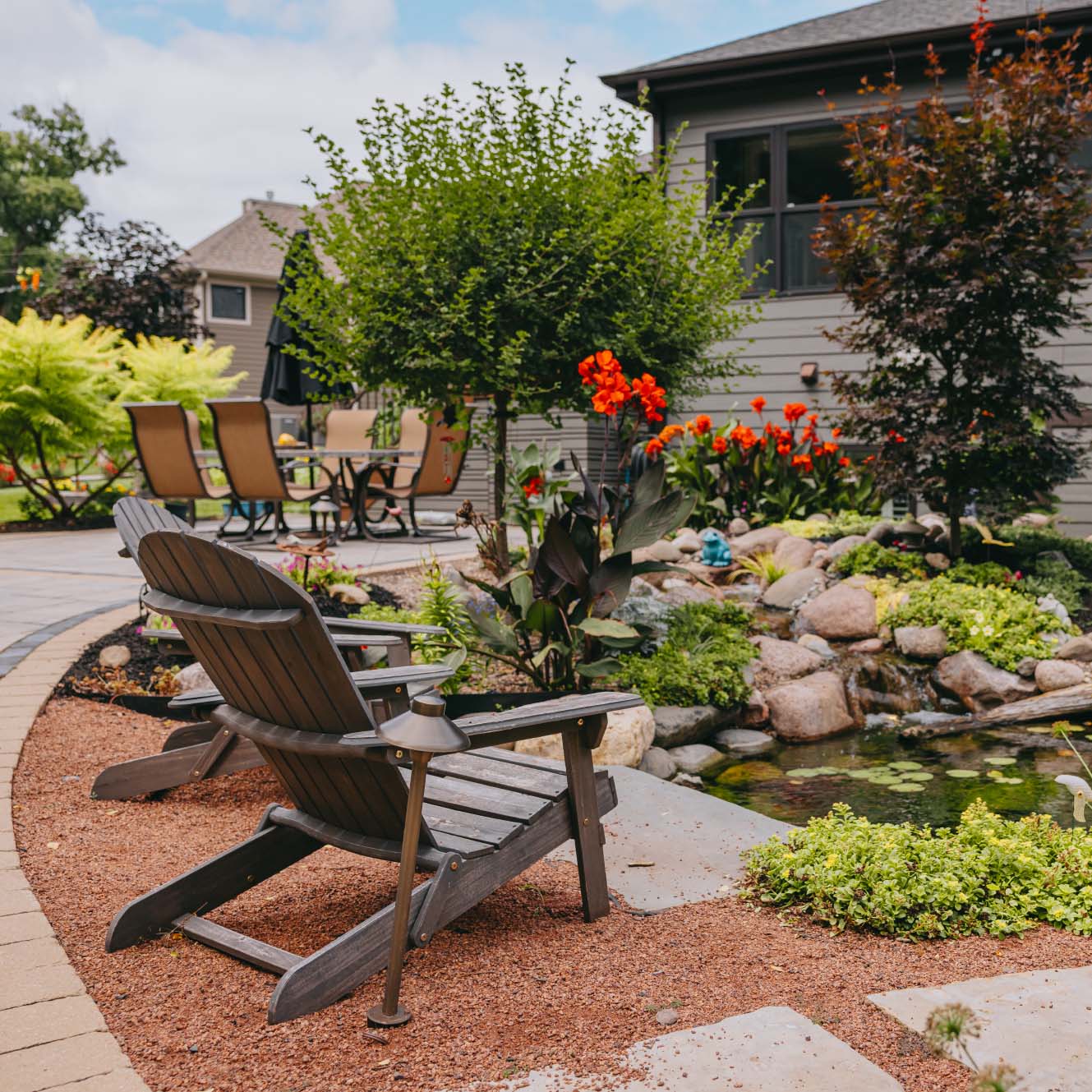 Backyard patio with Adirondack chairs overlooking pond and colorful garden in suburban Chicago.