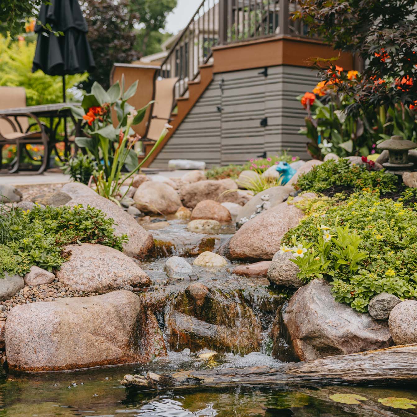 Backyard waterfall and pond surrounded by flowers, rocks, and a patio area in the Chicago suburbs.