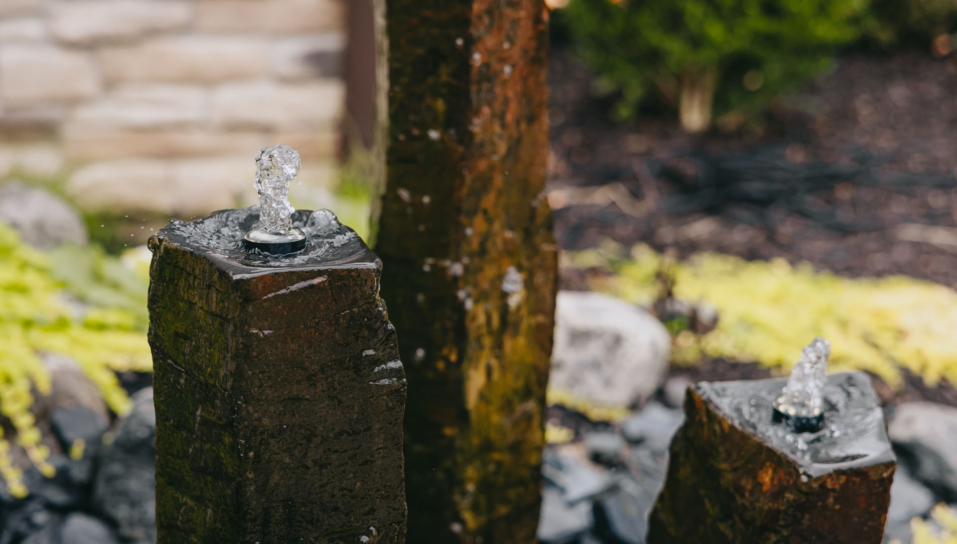 Detailed close-up of bubbling water feature on textured stone in a landscaped front yard, Chicago suburbs.