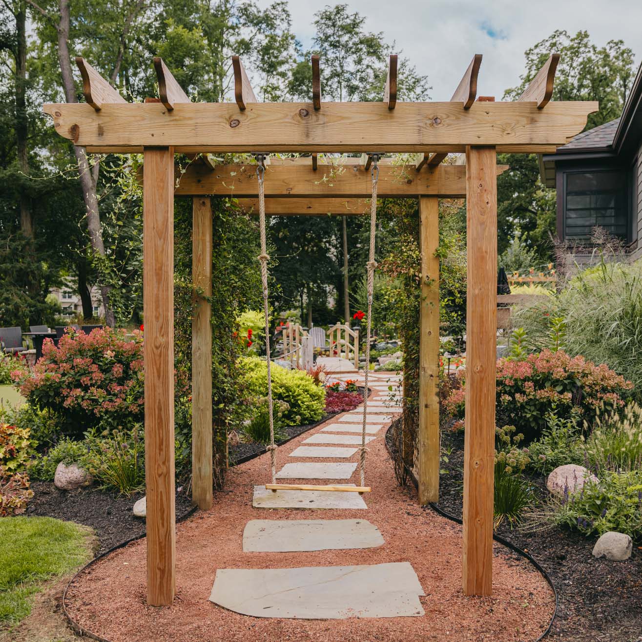 Wooden pergola with stone walkway leading through vibrant garden landscape in suburban Chicago.
