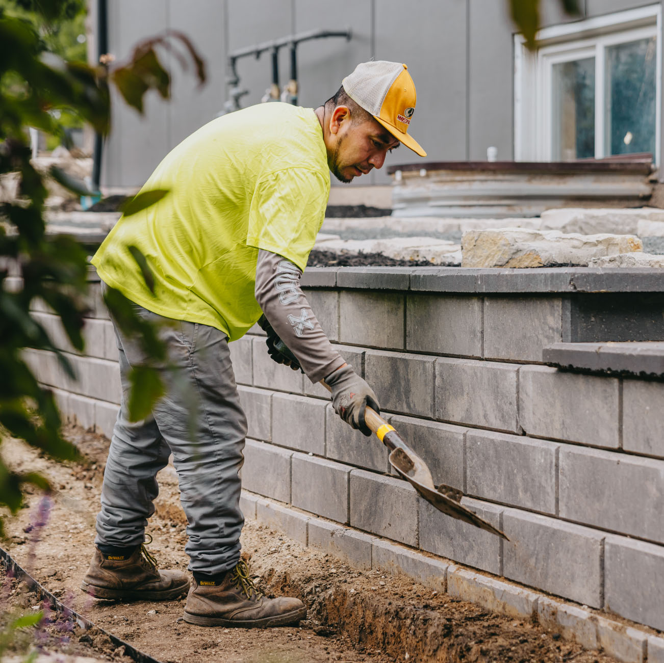 Worker building retaining wall with gray stone blocks for a landscape project, Chicago suburbs.