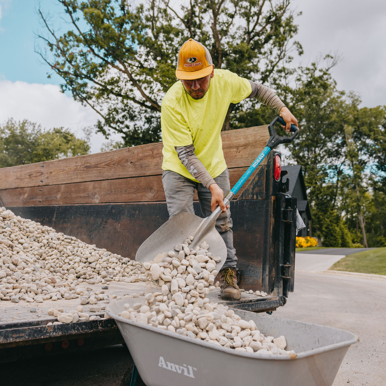 Landscaper transferring white stones into wheelbarrow for residential garden project, Chicago suburbs.