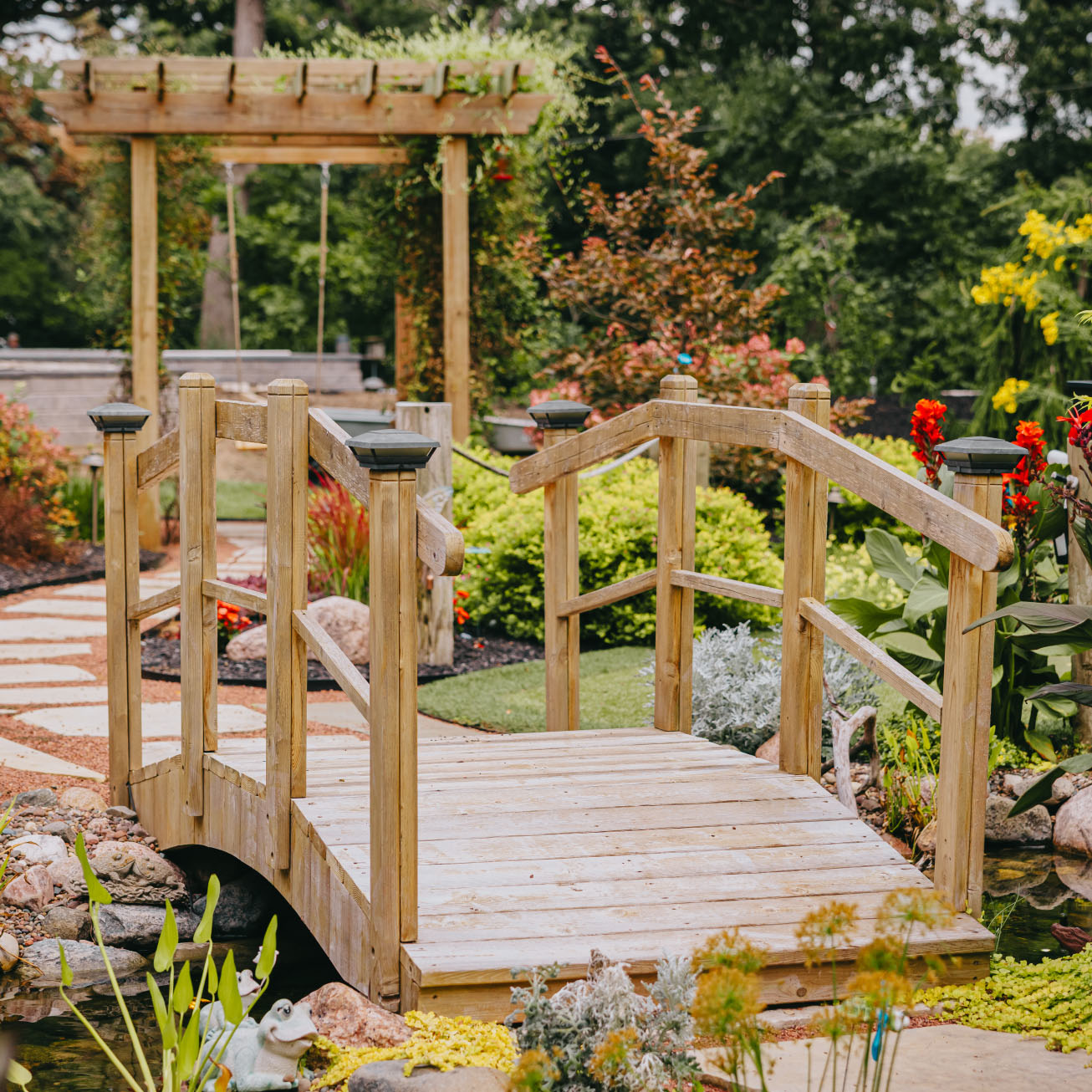Wooden garden bridge and swing path in a custom landscaped backyard, Chicago suburbs.