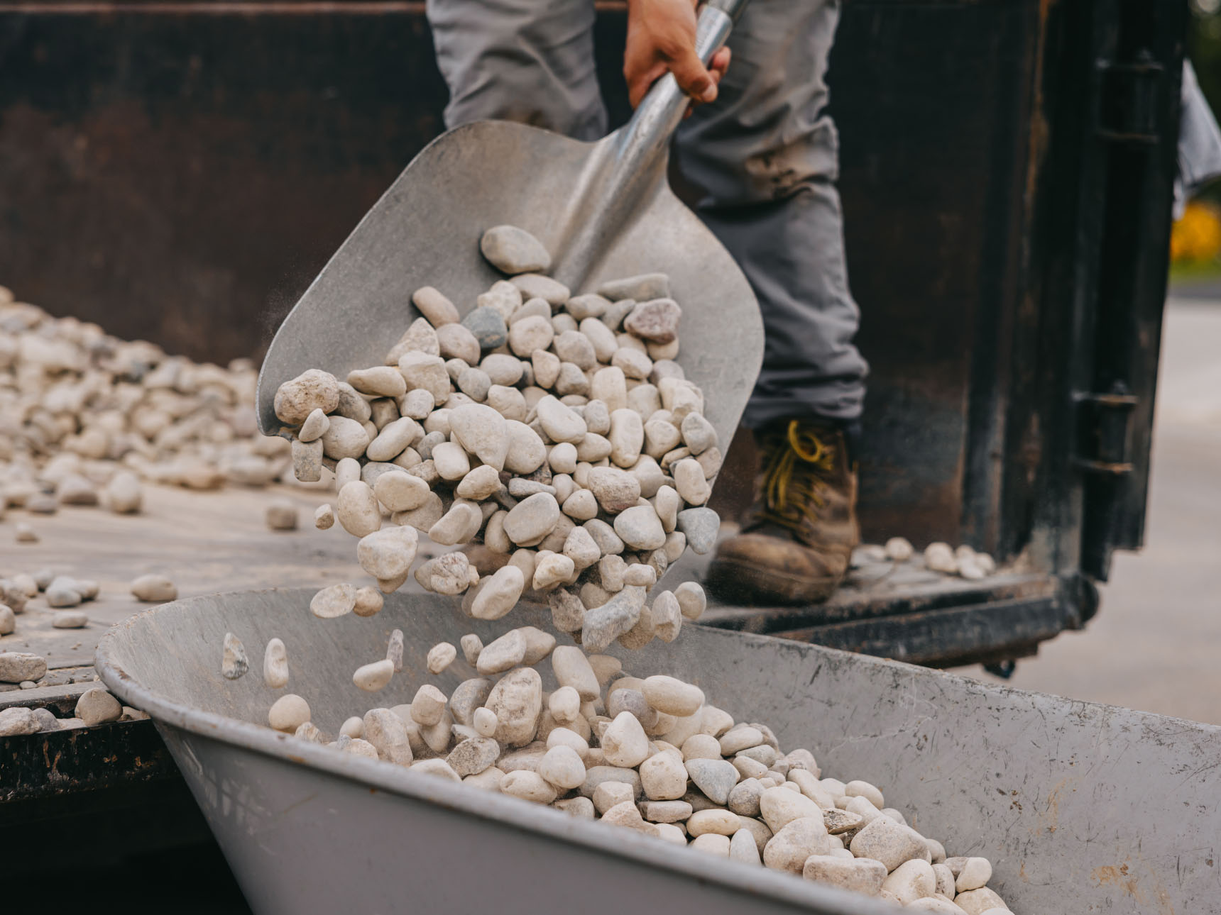 Worker shoveling decorative river rocks into wheelbarrow for landscape project, Chicago suburbs.