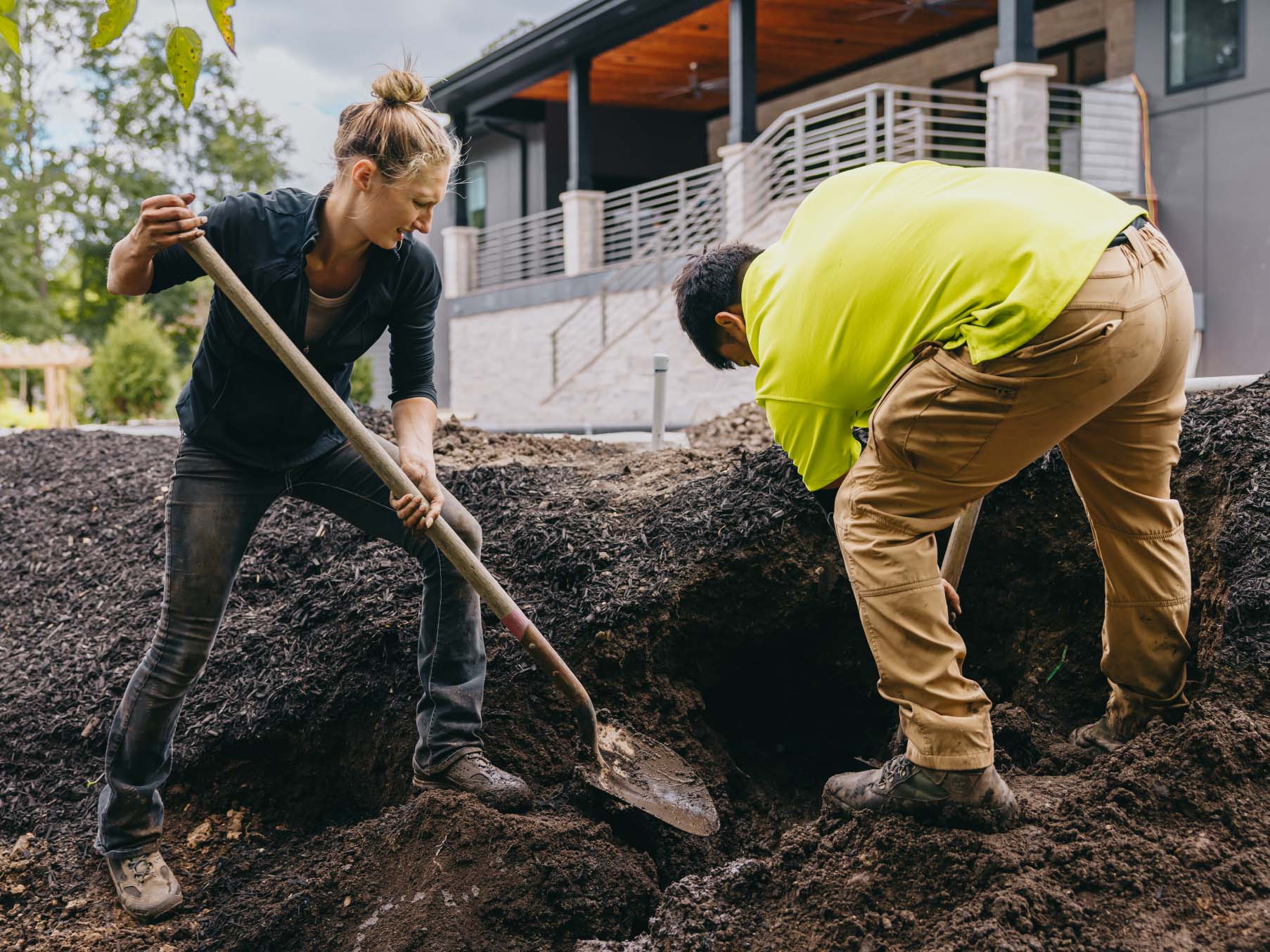 Landscapers digging soil and shaping a new outdoor garden bed near a modern home in the Chicago suburbs.