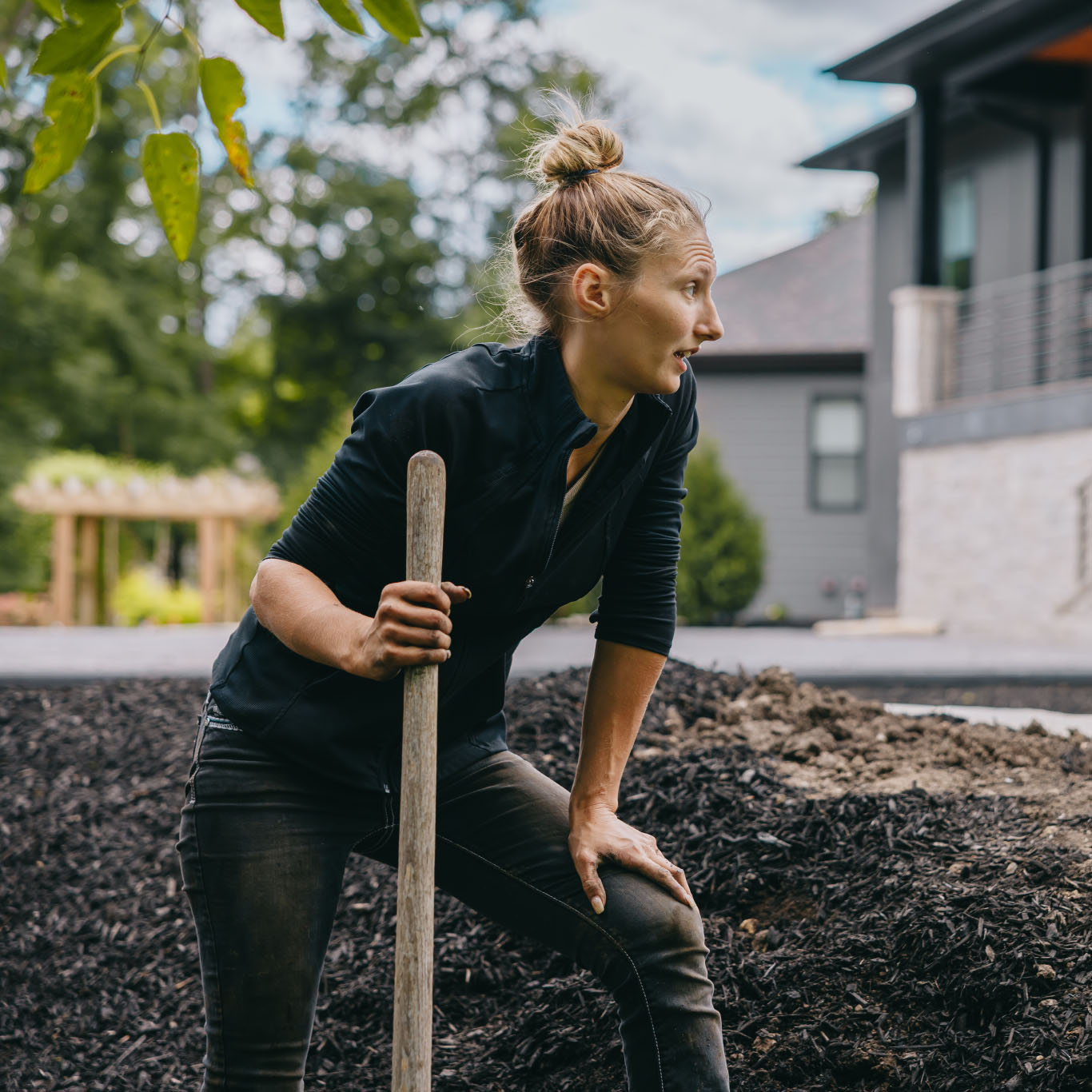 Female landscaper taking a break while working with shovel and mulch near modern home