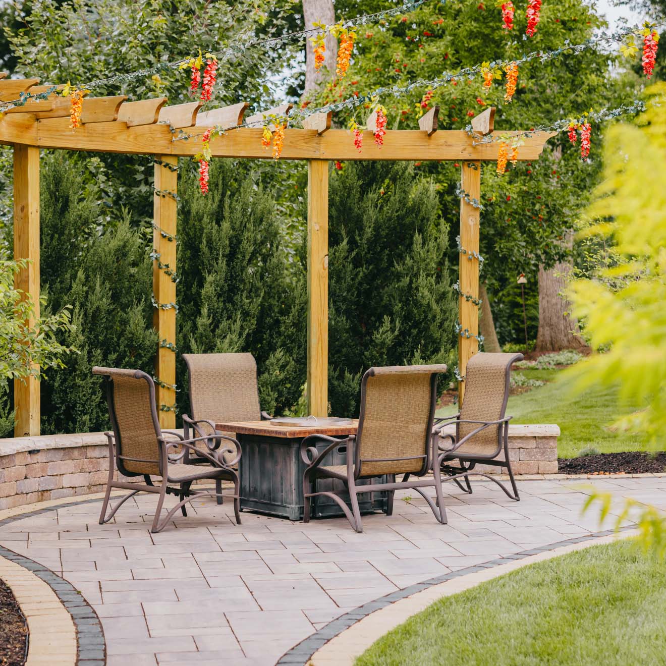 Patio seating area under wooden pergola with hanging string lights and lush landscaping