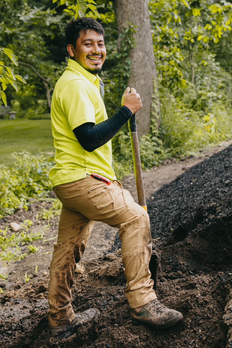 Smiling landscaper holding a shovel while working on a garden project for Custom Scapes and Designs in suburban Chicago.