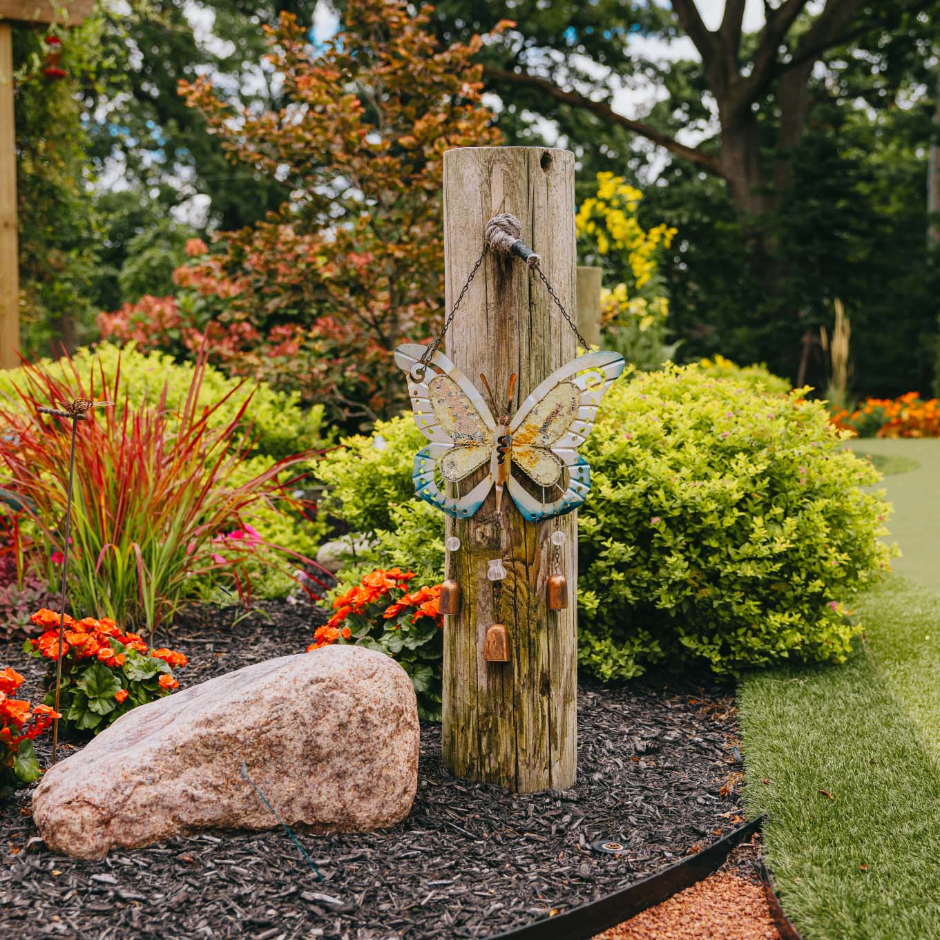 Decorative butterfly ornament mounted on a garden post surrounded by colorful plants and flowers in suburban Chicago.