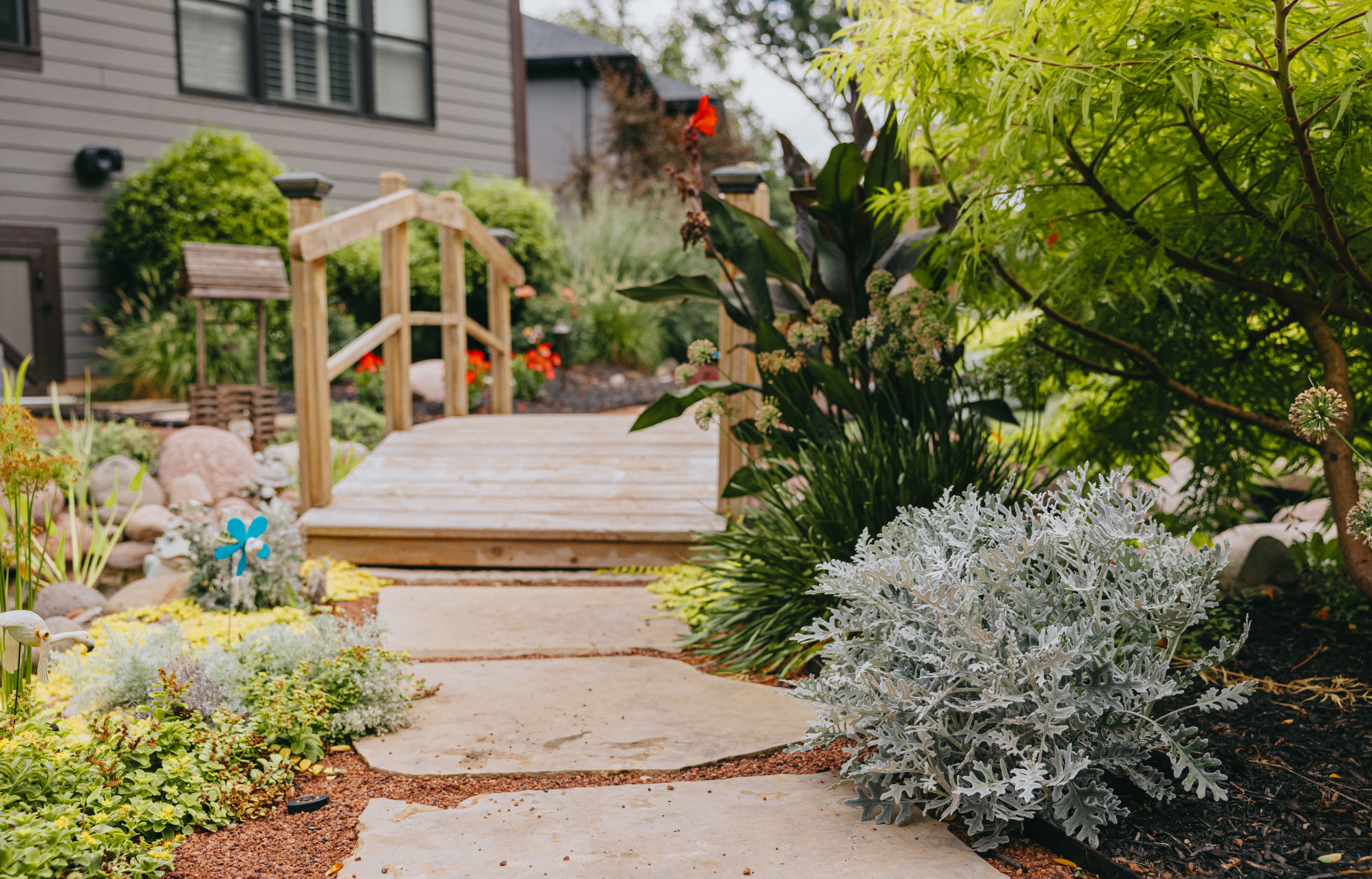 Wooden garden bridge leading through lush landscaping in suburban backyard